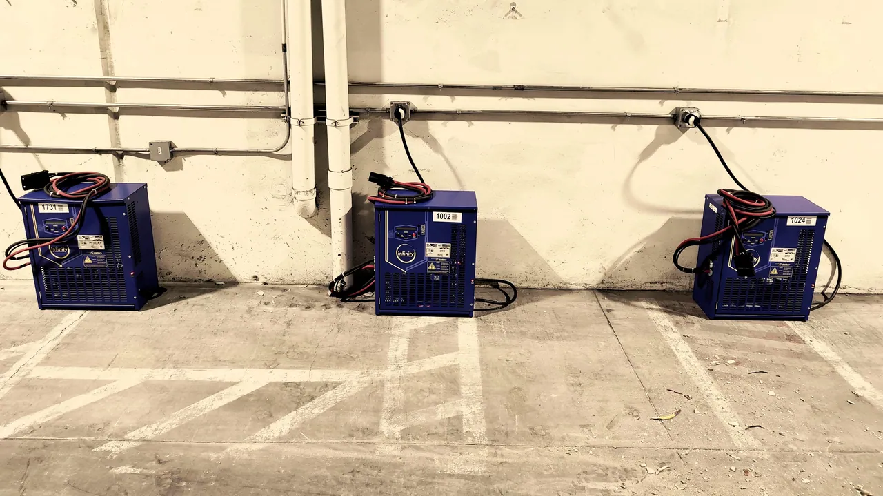 Three forklift battery chargers along a warehouse wall