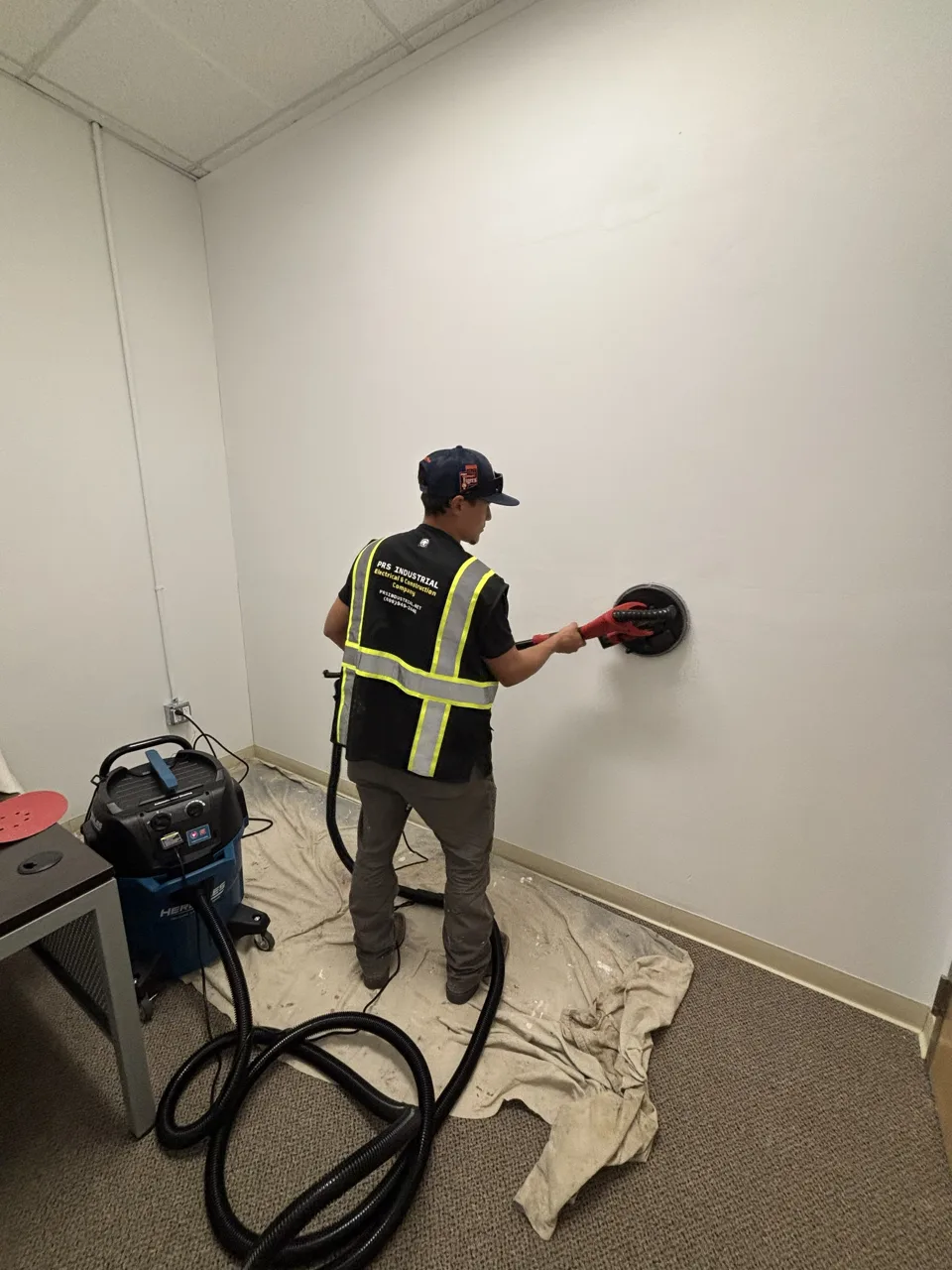 Technician sanding an interior wall during a facility repair